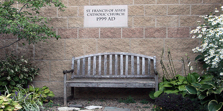 Bench underneath St. Francis sign, surrounded by rocks and greenery