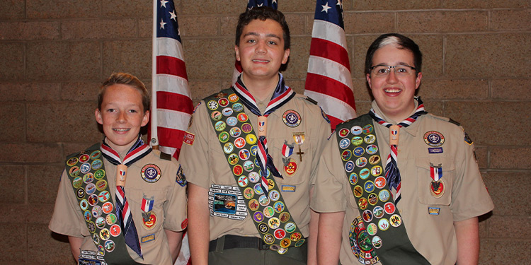 Three young boy scouts pose in front of American flags