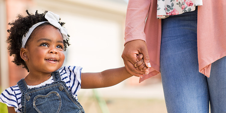 Young toddler girl smiles and holds her mom's hand