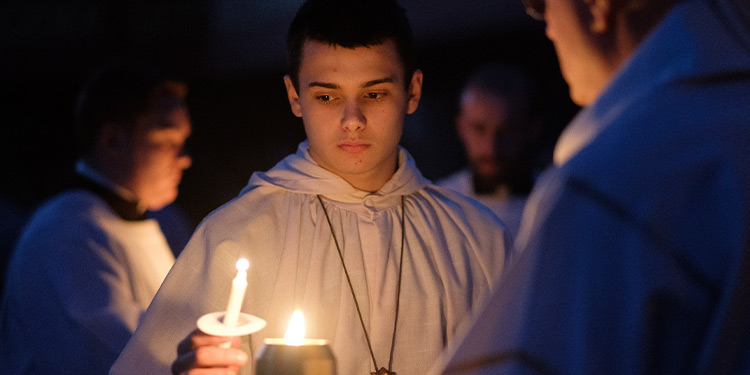 Young man in white robe holds a lit candle