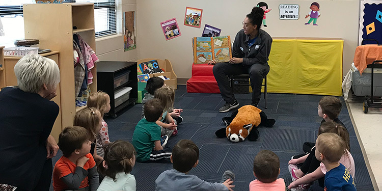 Preschool students sit on floor while teacher reads a story to them