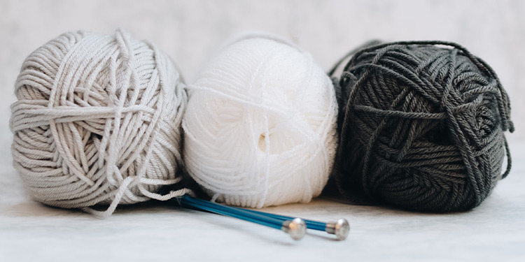 Three balls of yarn with two knitting needles tucked underneath them